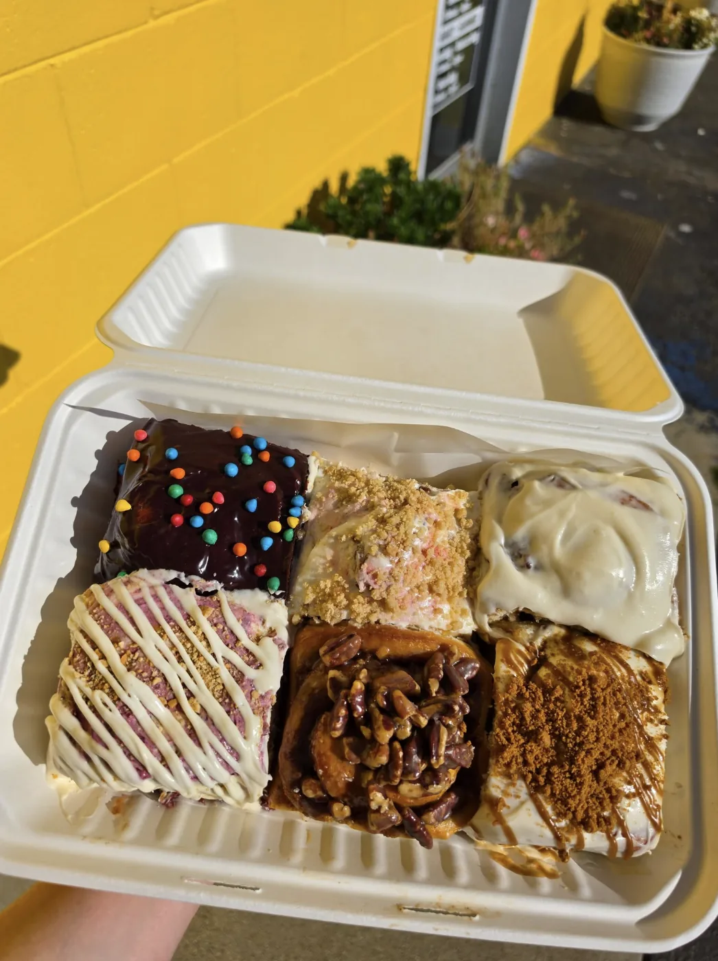 A six-pack of Mellow Yellow cinnamon rolls in a takeaway box, each a different flavor